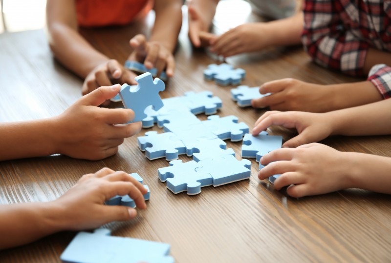 Little children playing with puzzle at table, focus on hands. Unity concept