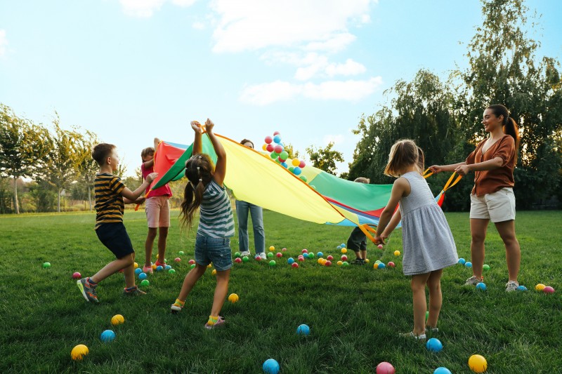 Group of children and teacher playing with rainbow playground pa