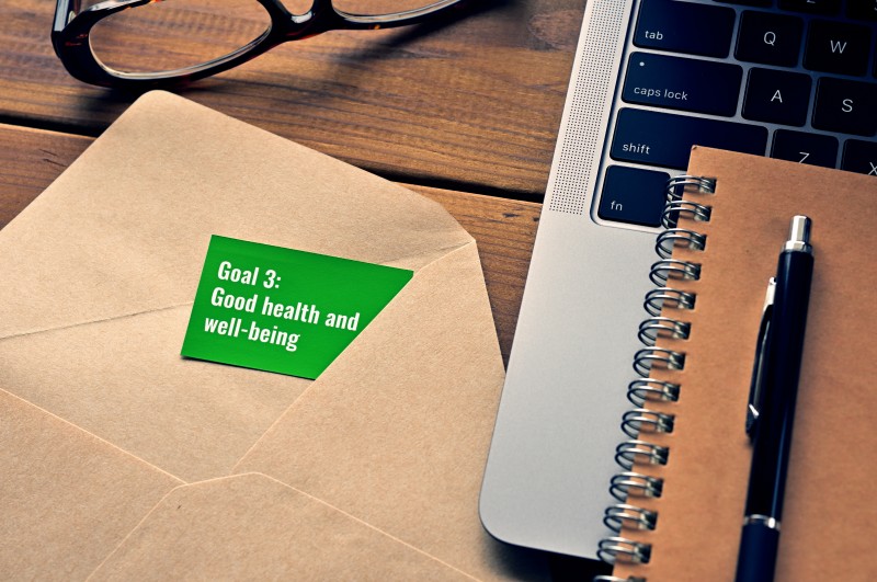 There is a card with the word of Goal 3: Good health and well-being which is one of the goals of the Sustainable Development Goals.It's by the envelope or laptop computer.