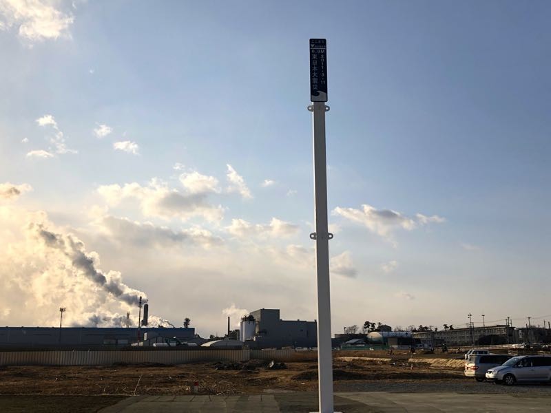 「がんばろう！石巻」看板の傍に建つ、6.9メートルの津波高さを示すポール。 